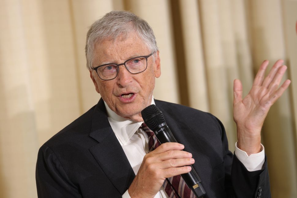 Man in black suit sits on stage speaking into mic