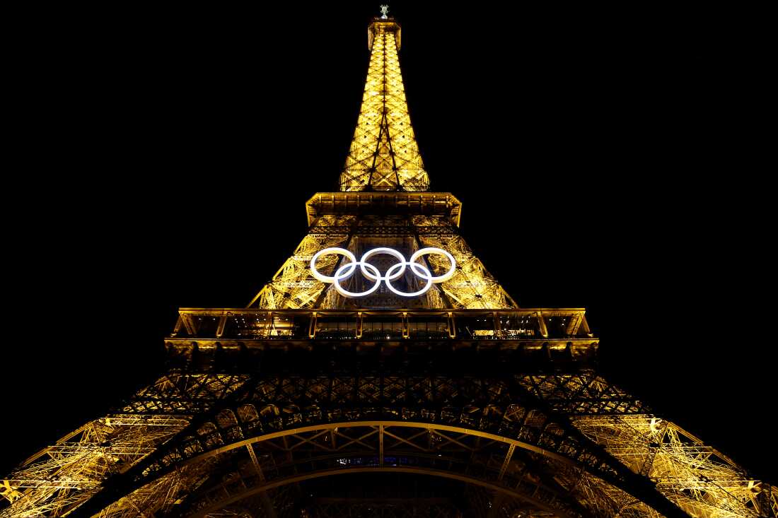 A view of the Olympic rings beneath the Eiffel Tower, lit up at night.